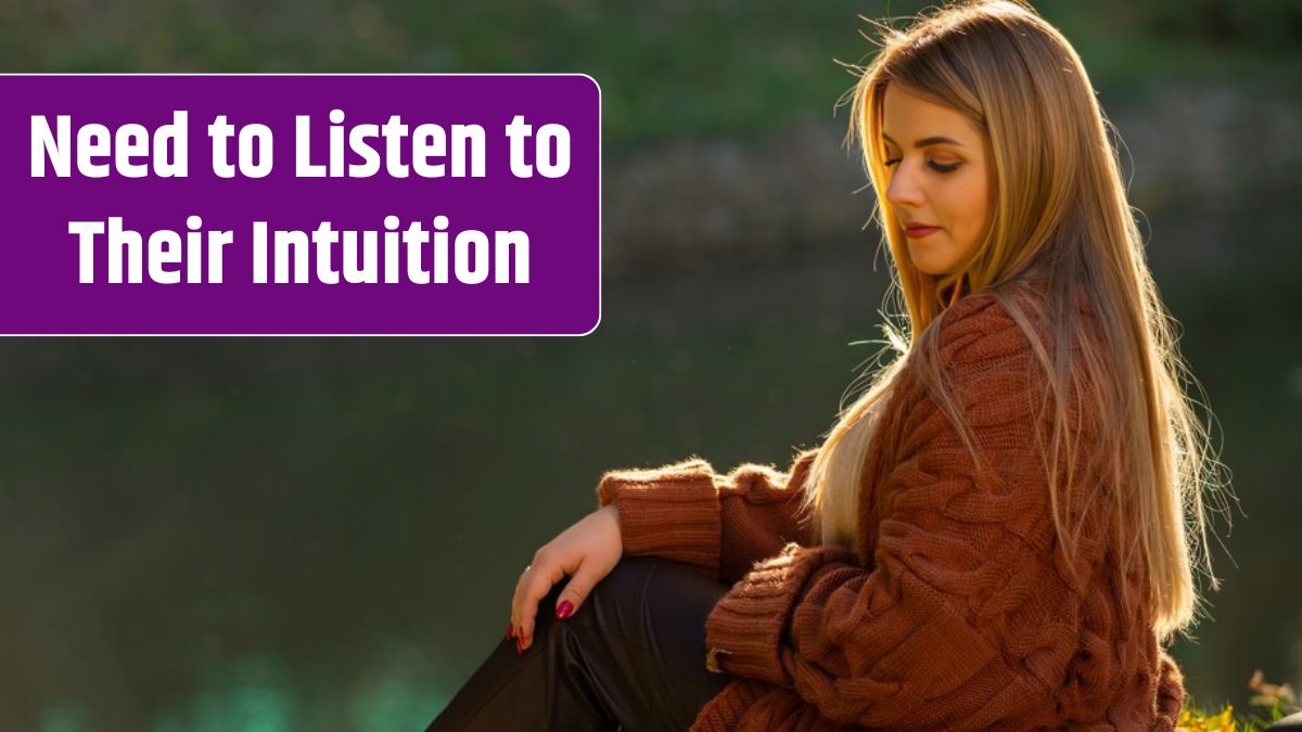 Serene young woman relaxing in evening light sitting on the grass above a pond in an autumn park backlit by the golden sun.